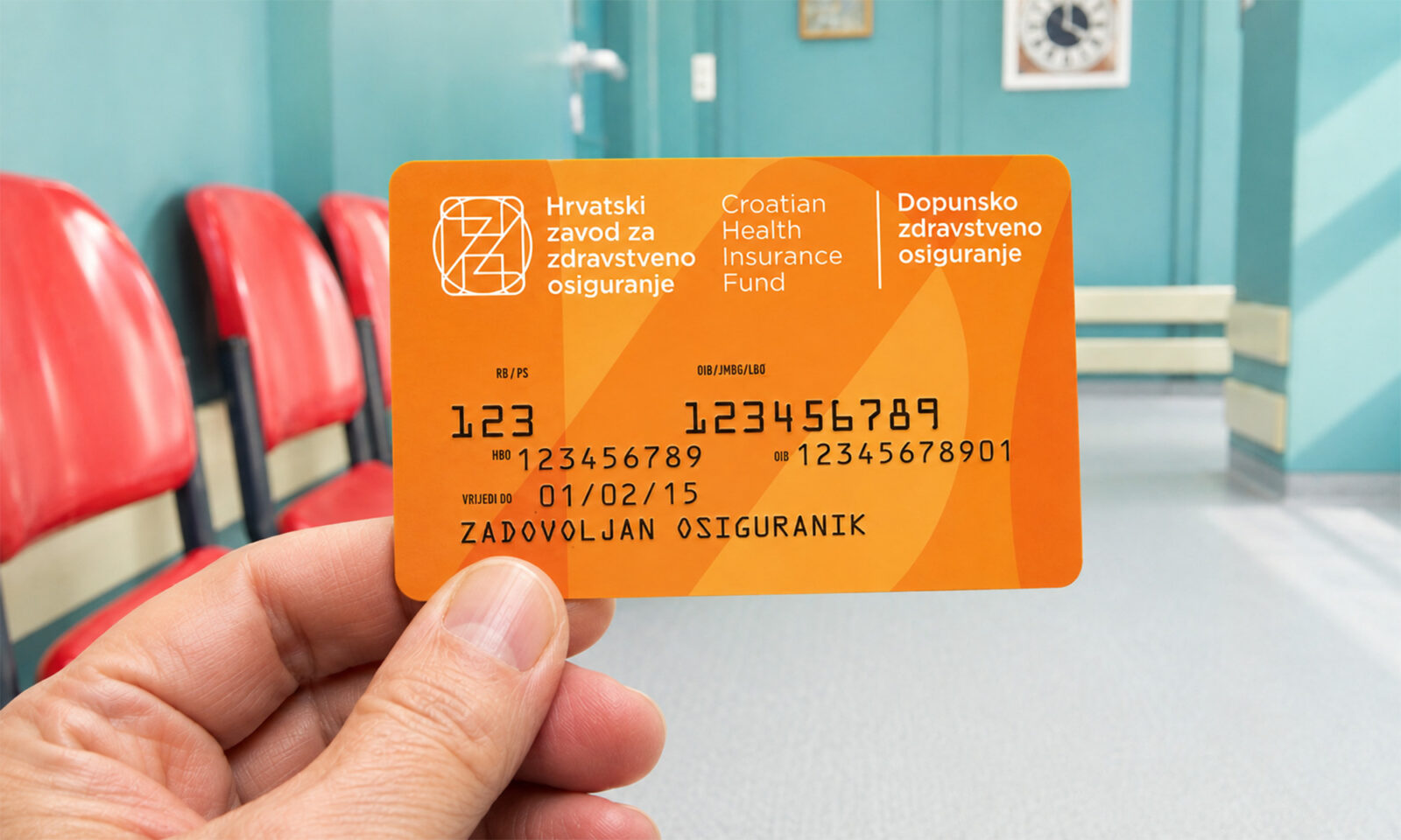 Ruka drži narančastu karticu HZZO-ova dopunskog zdravstvenog osiguranja u svijetloj bolničkoj čekaonici s crvenim stolicama.