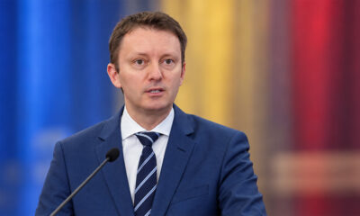 Siegfried Mureșan na konferenciji za novinare, ispred zamućene pozadine u bojama rumunjske zastave.