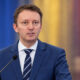 Siegfried Mureșan na konferenciji za novinare, ispred zamućene pozadine u bojama rumunjske zastave.