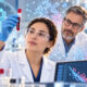 Znanstvenica u laboratoriju promatra epruvetu s uzorkom krvi, dok iza nje tim istraživača i digitalni prikazi biomarkera starenja simboliziraju pomlađivanje biološke dobi.