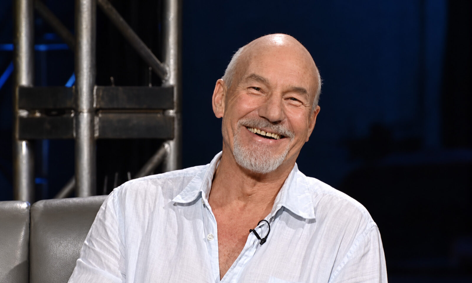 Glumac Patrick Stewart nasmiješen sjedi u televizijskom studiju.