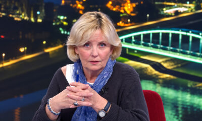Višnja Stanišić u televizijskom studiju, s plavim šalom i sklopljenim rukama u kojima drži olovku.
