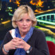Višnja Stanišić u televizijskom studiju, s plavim šalom i sklopljenim rukama u kojima drži olovku.
